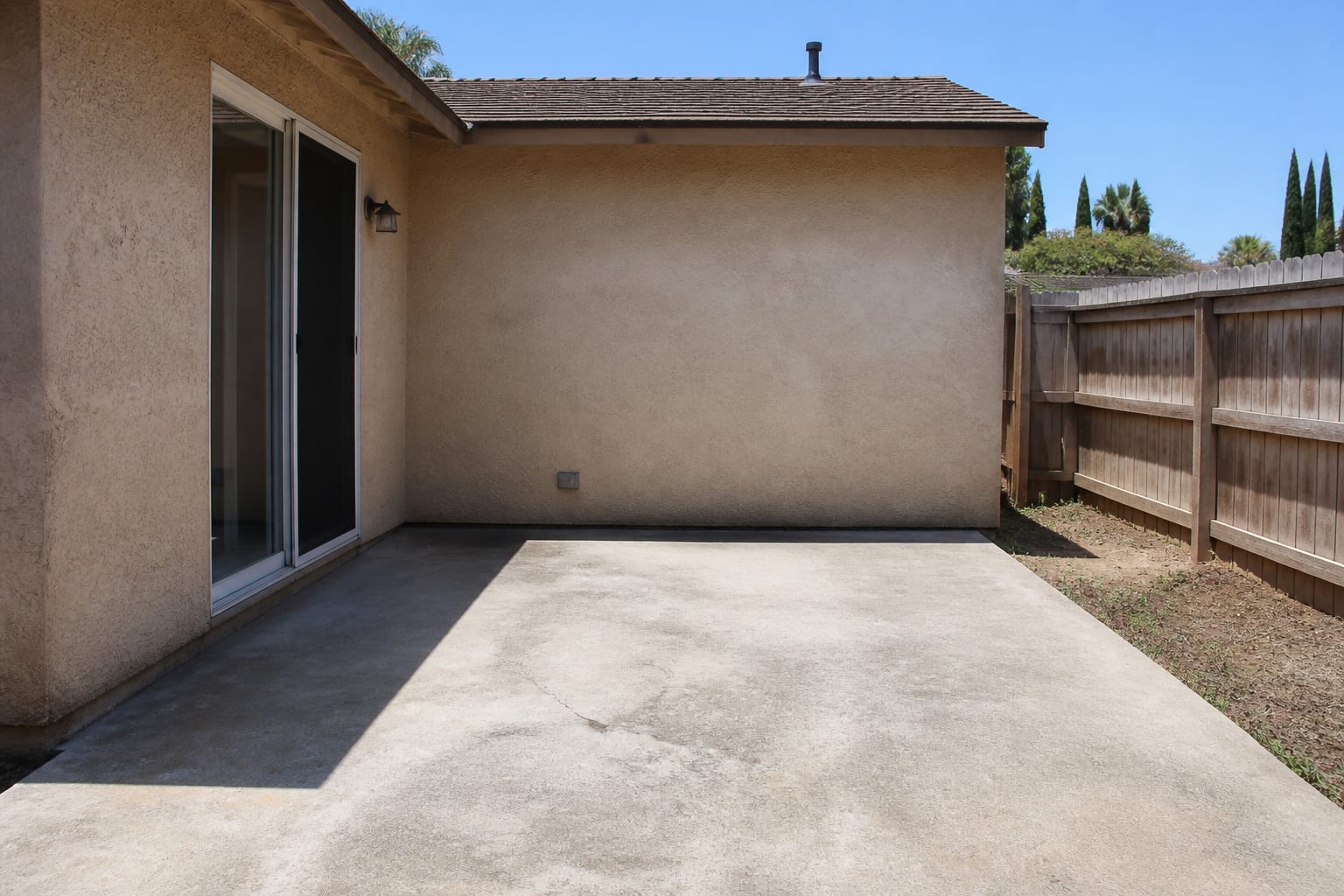 An empty concrete patio with no furniture against a beige house wall