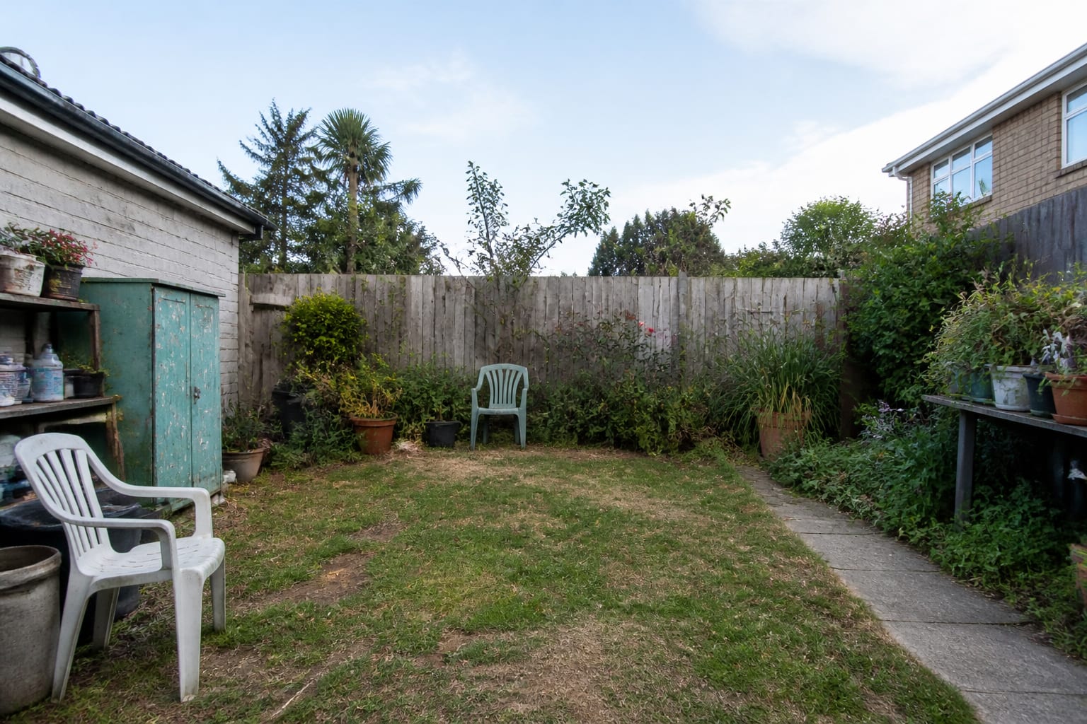 under designed garden corner with patchy lawn, plain fence, no path, and no clear place for a greenhouse or seating