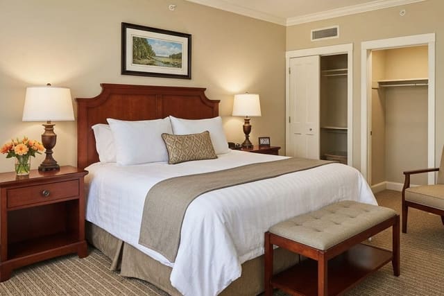 warm guest bedroom with upholstered headboard, layered lamps, luggage bench, and calm neutral storage wall