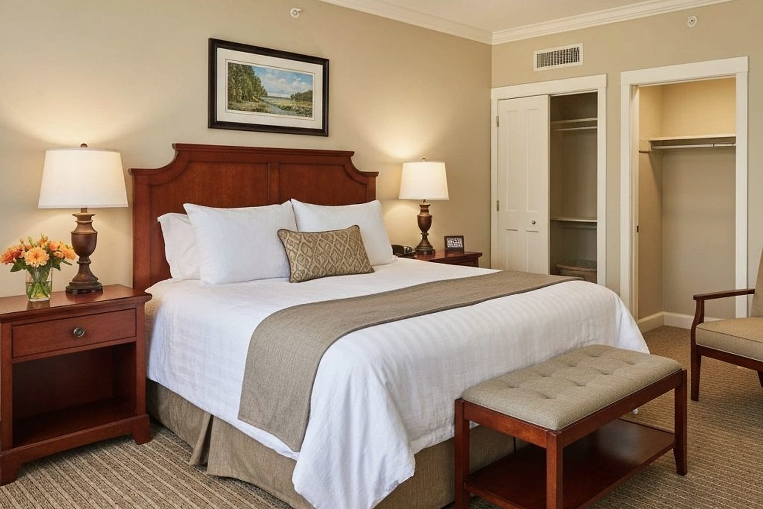warm guest bedroom with upholstered headboard, layered lamps, luggage bench, and calm neutral storage wall