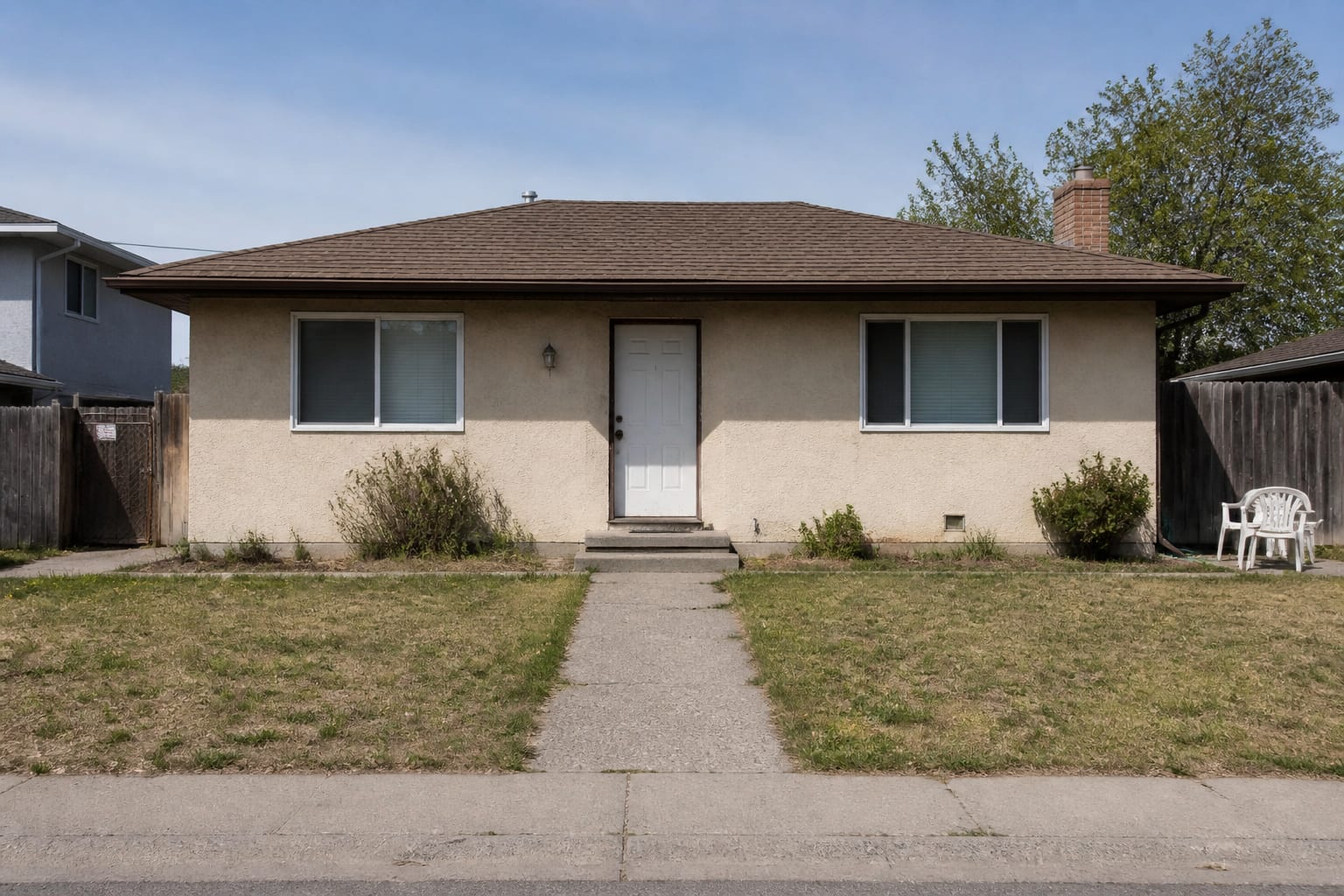 beige house exterior with undersized porch lights, faded front door, sparse foundation shrubs, plain walkway, and little contrast from the street.