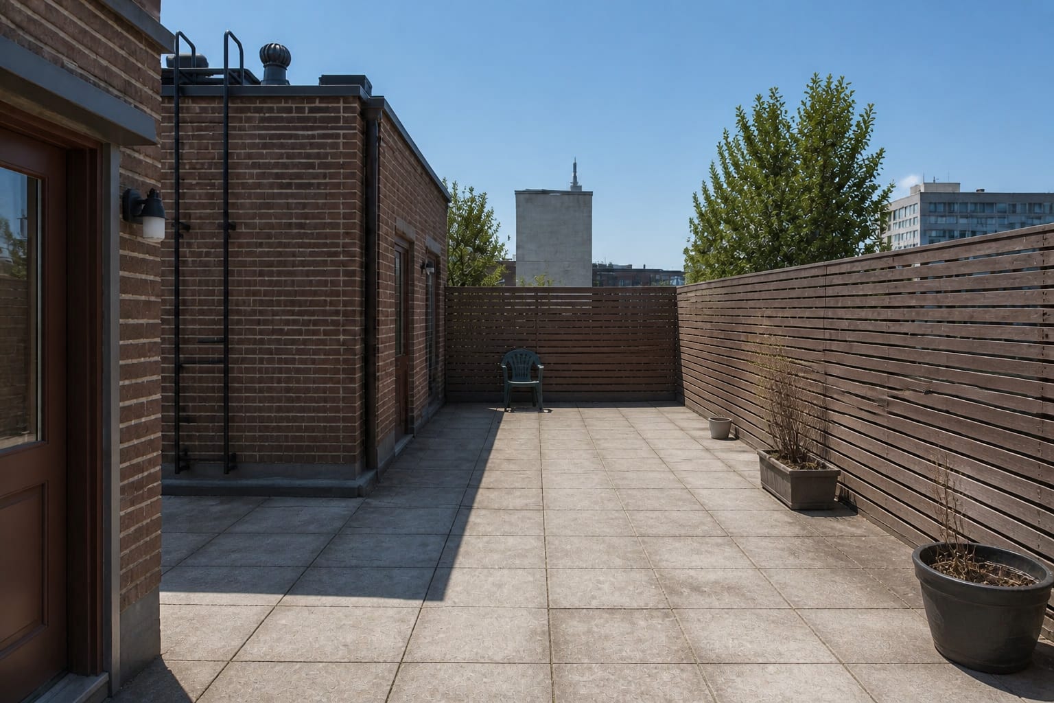Under-designed roof terrace with blank pavers, exposed parapet walls, scattered chairs, harsh sun, and no planting or privacy strategy.
