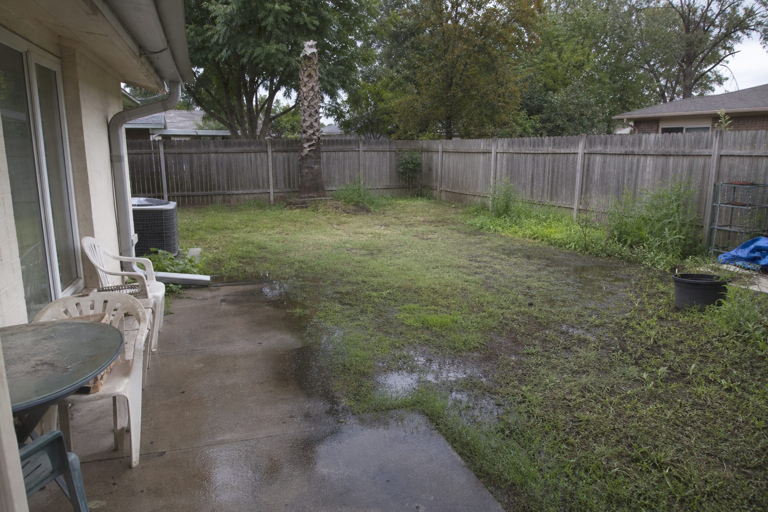 flat backyard lawn with puddles near the house, exposed downspout discharge, and no defined dry seating zone