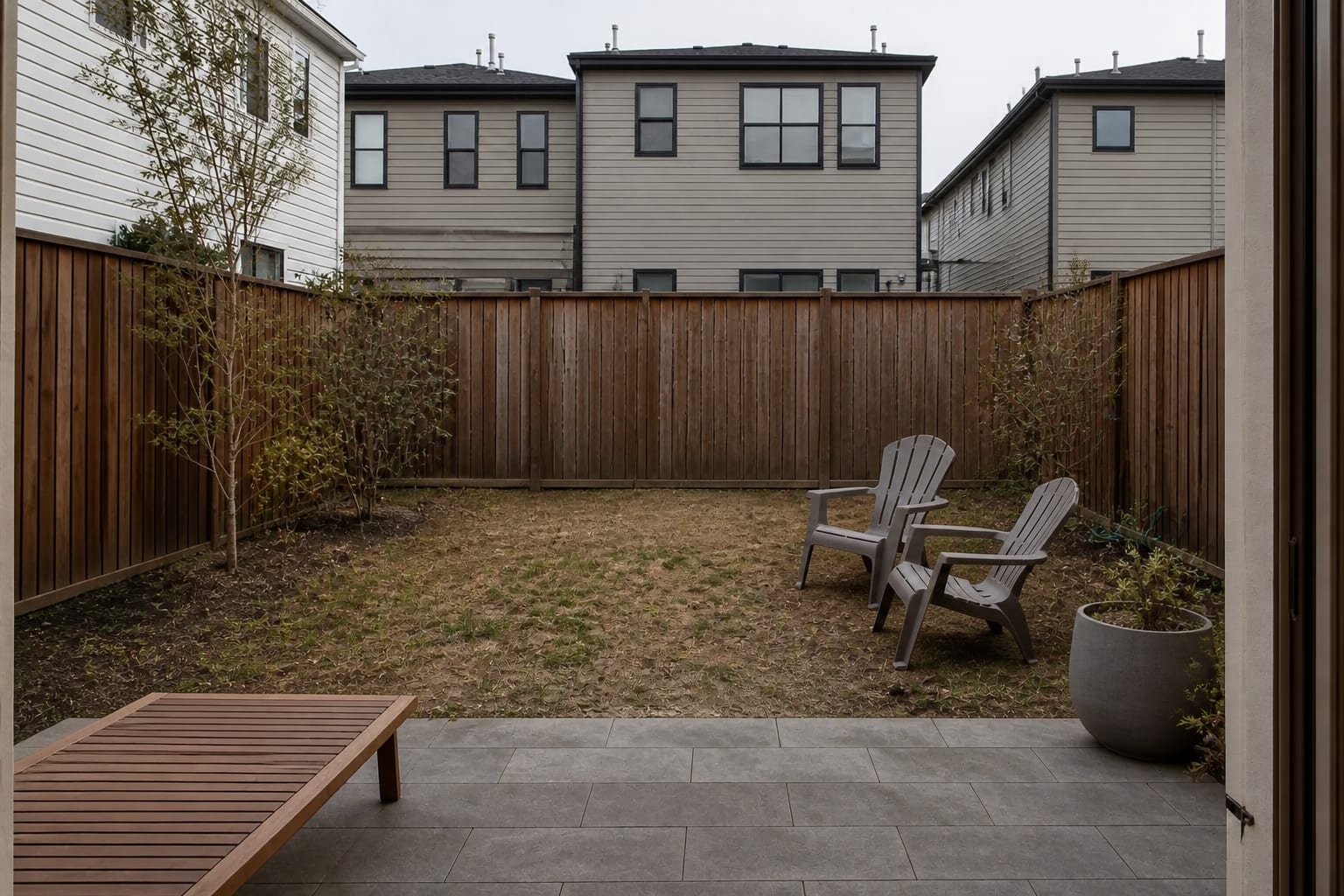 plain backyard fence with scattered chairs, patchy lawn, and no clear visual destination from the patio door