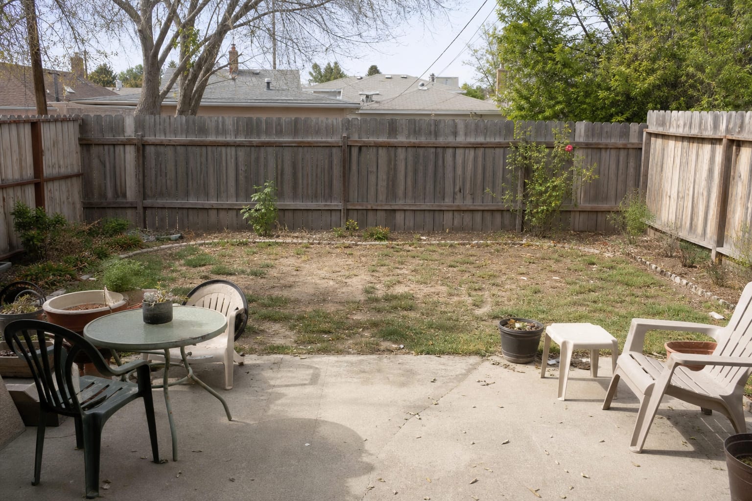 plain backyard fence with scattered chairs, patchy lawn, and no clear visual destination from the patio door