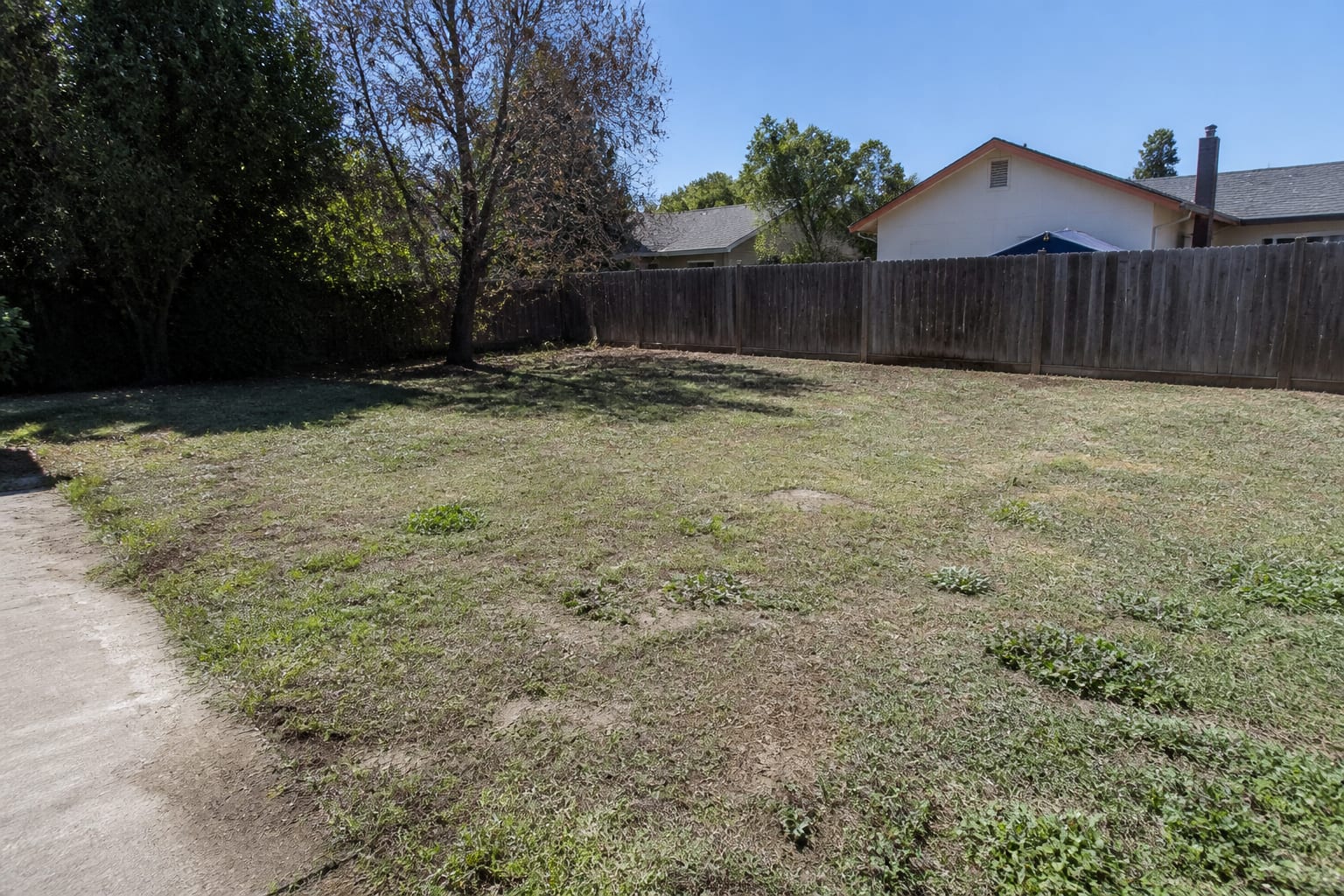 A bare, ungraded backyard with patchy grass, exposed dirt, and no defined beds or patio