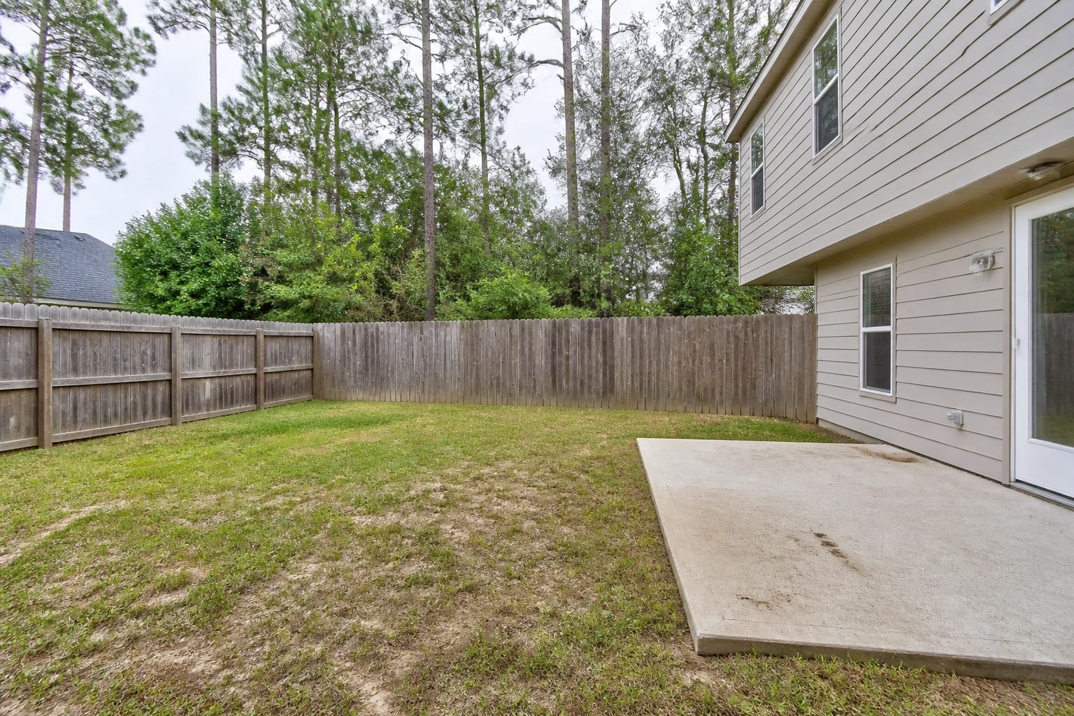 Plain grass backyard with no sports surface, overgrown lawn and unused concrete pad along the side of the house