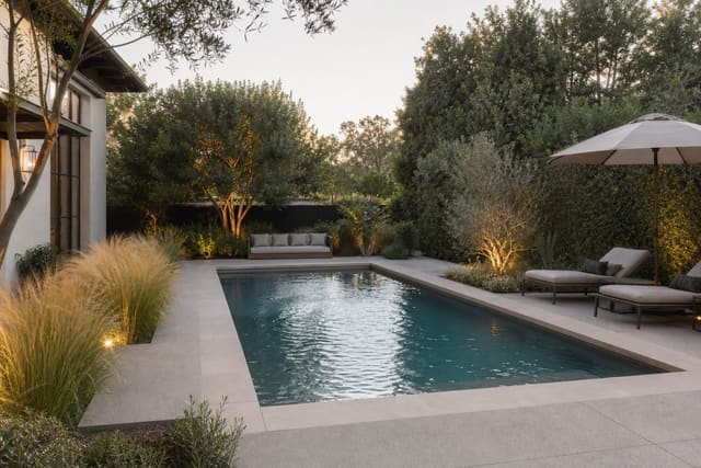 compact backyard pool with pale coping, grasses, shaded loungers, and a clear path around the water