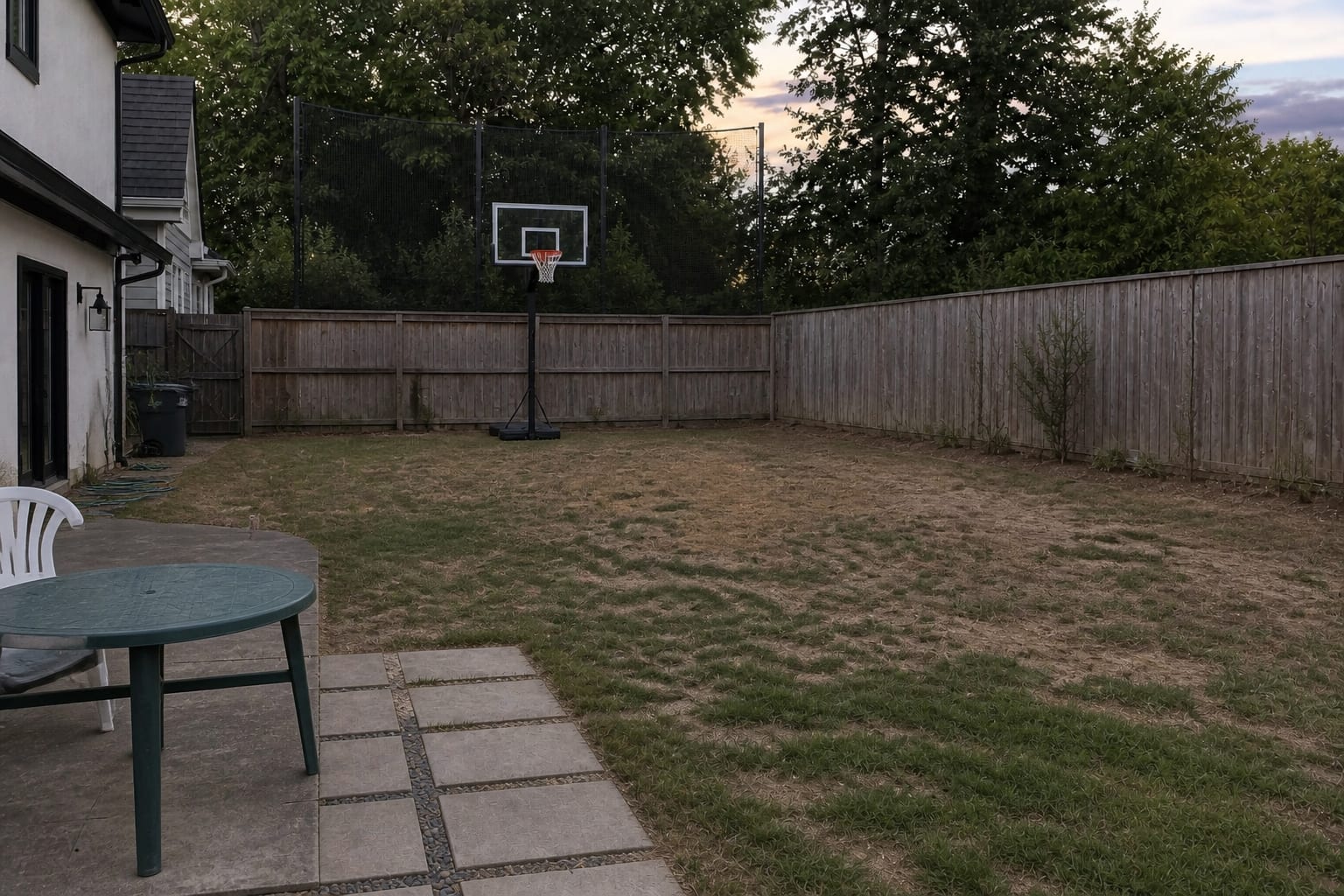 Under-designed backyard lawn with patchy grass, no active play zone, exposed fence line, and scattered outdoor toys near the patio.