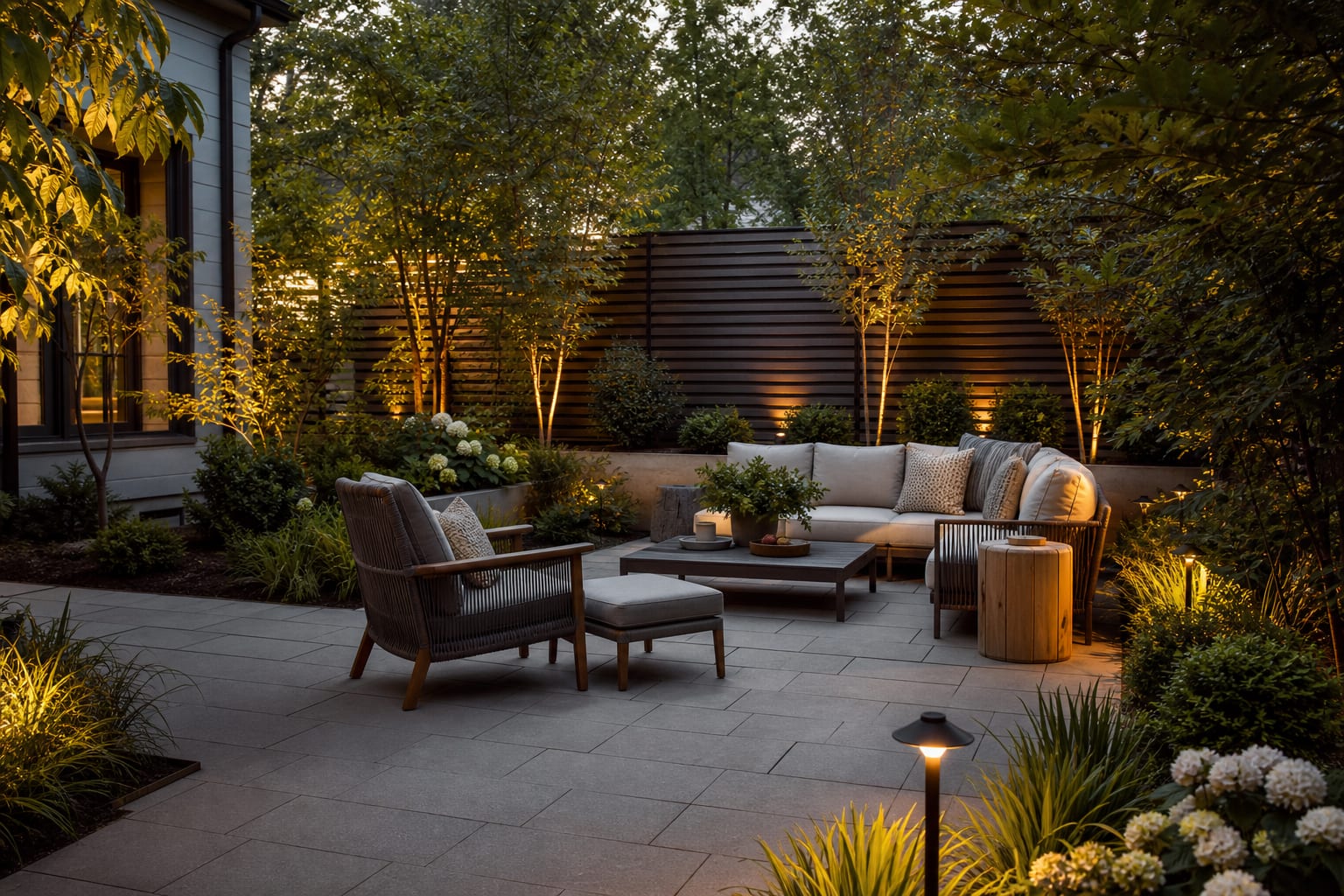 backyard lounge zone with pavers underfoot, layered planting edge, privacy screen, and warm path lighting