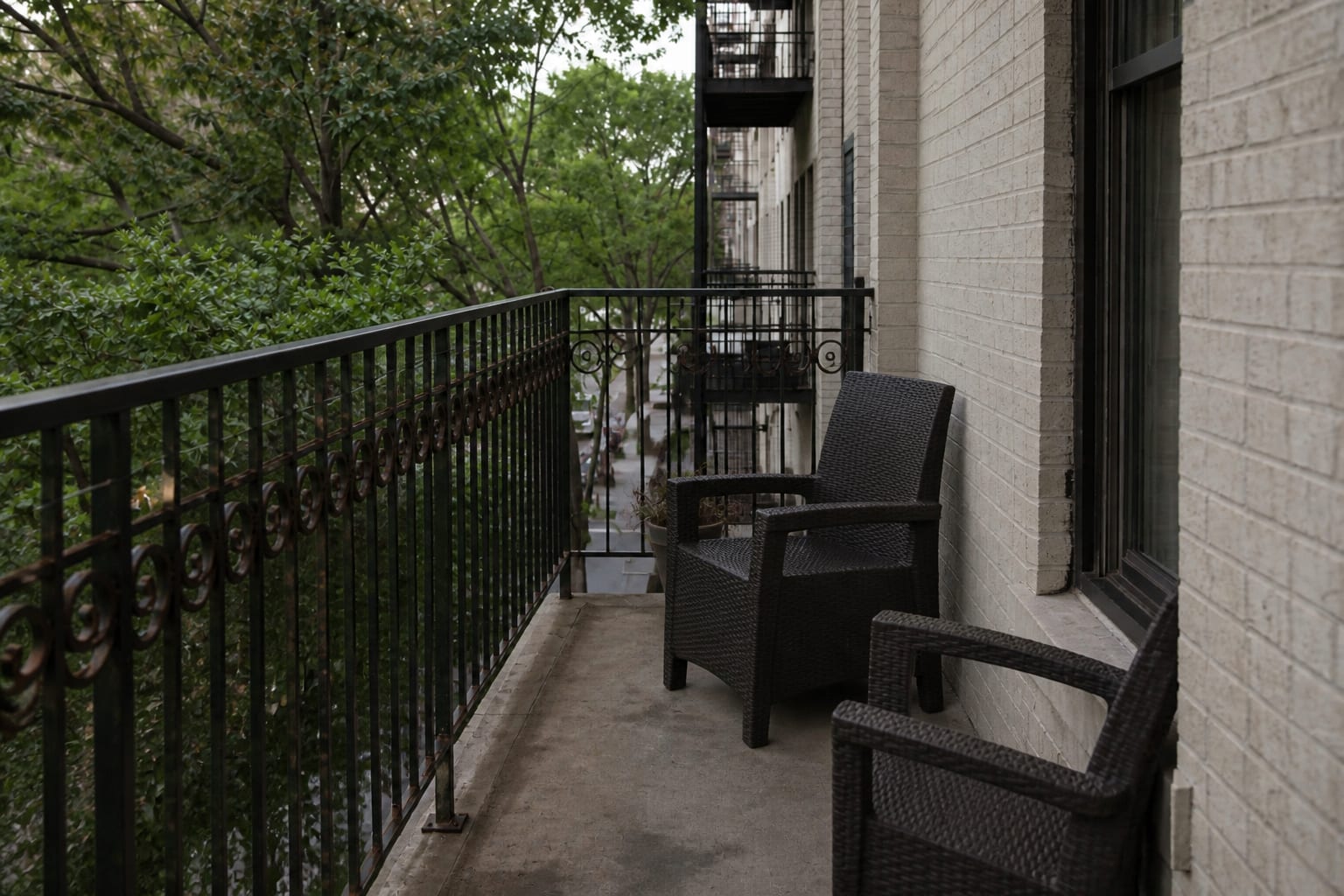 narrow apartment balcony with oversized outdoor chairs, no usable table surface, bare railing, and a blocked walking path
