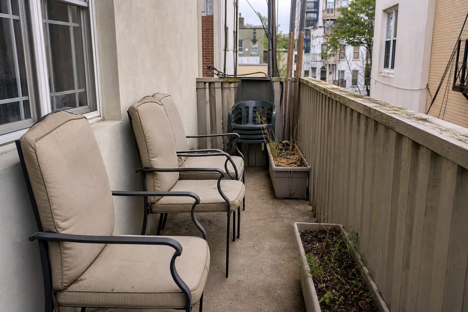 narrow apartment balcony with oversized outdoor chairs, no usable table surface, bare railing, and a blocked walking path