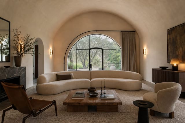 living room with a barrel vault ceiling, low curved sofa, large wool rug, warm sconces, and furniture centered beneath the arch