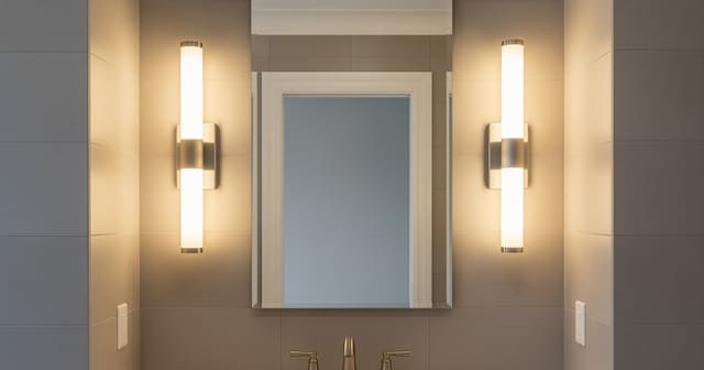 A bathroom mirror flanked by two vertical sconces at face level with warm-white LEDs