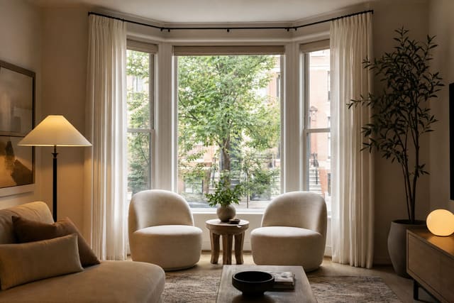 living room bay window with two low chairs, a small round table, full length curtains, and daylight kept open across the glass