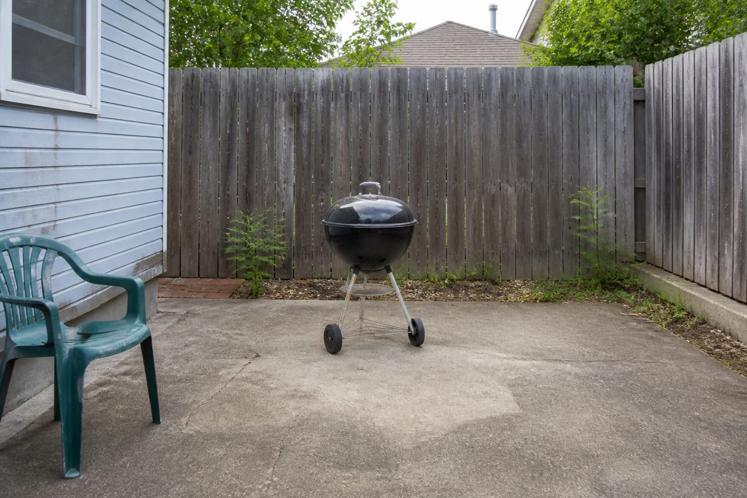 Plain concrete patio corner with a lone kettle grill and no counter or storage before redesign