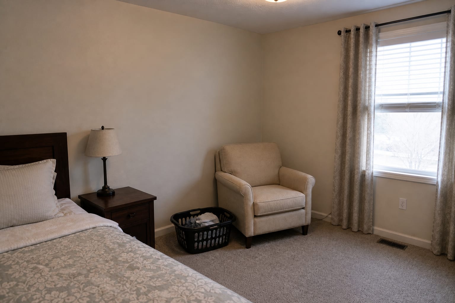 Bedroom corner with a laundry basket, unused accent chair, no side table, and cold overhead light.