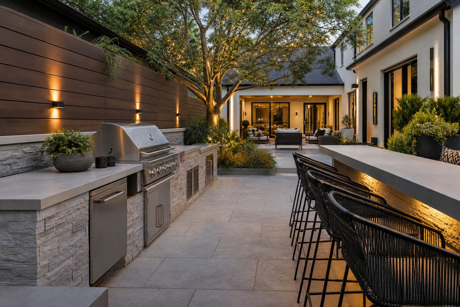 linear built-in grill wall with side counter, bar ledge, porcelain pavers, black metal stools, and a clear path to the house