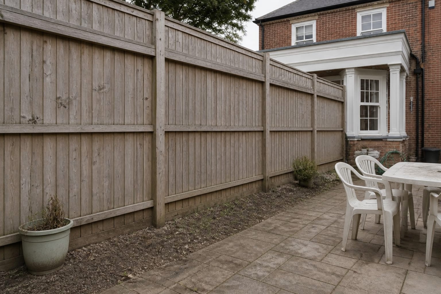 Plain timber garden fence with exposed boards, narrow bare soil strip, and no vertical planting to soften the boundary.