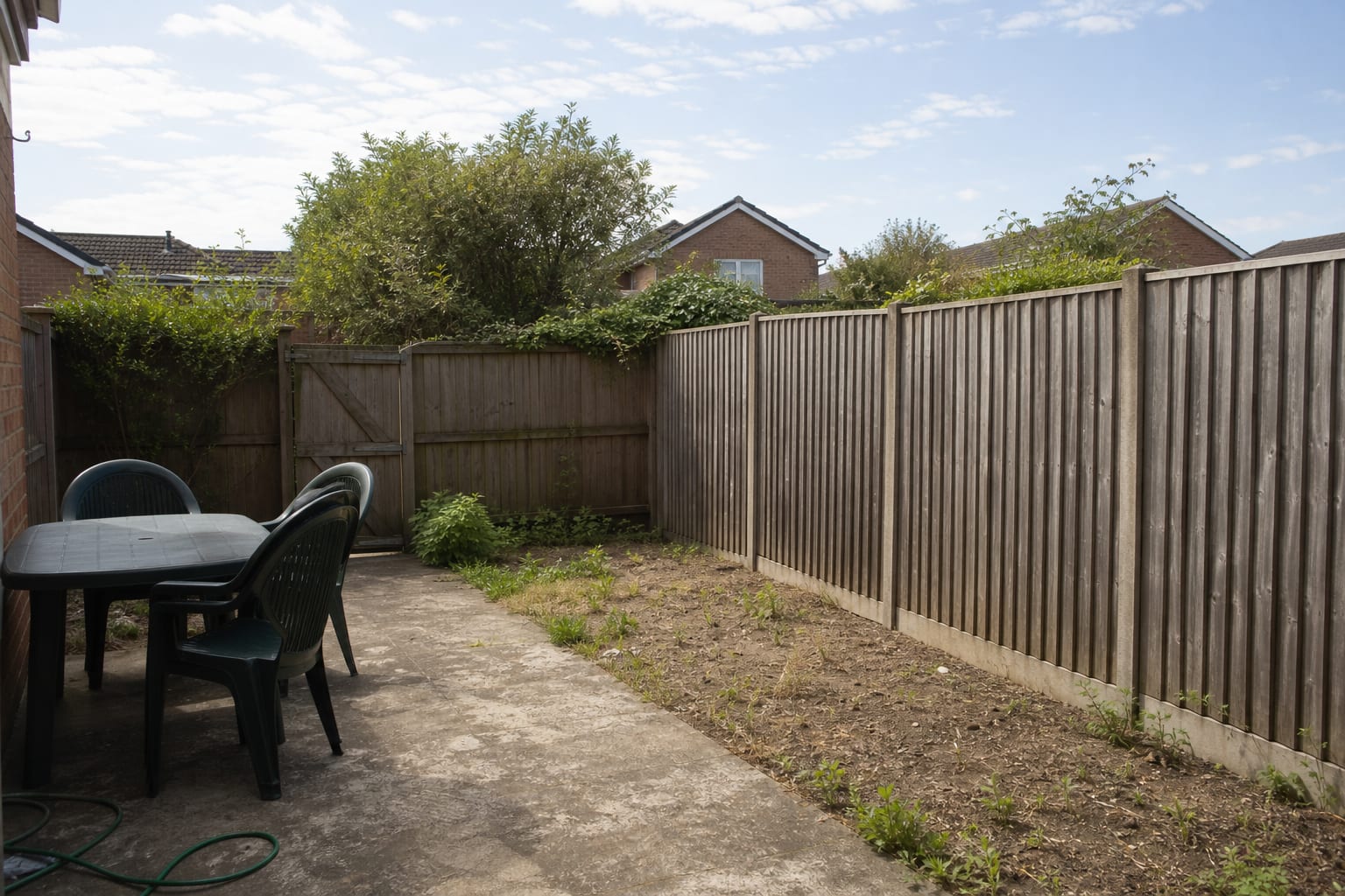 Plain timber garden fence with exposed boards, narrow bare soil strip, and no vertical planting to soften the boundary.