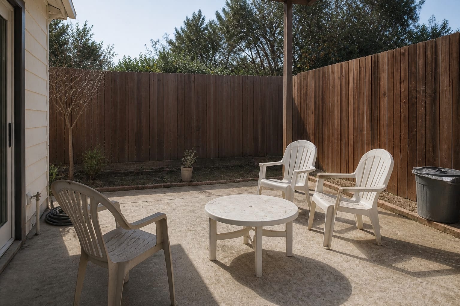 under-designed concrete patio with mismatched plastic chairs, harsh sun, empty fence line, and no defined coastal seating zone.
