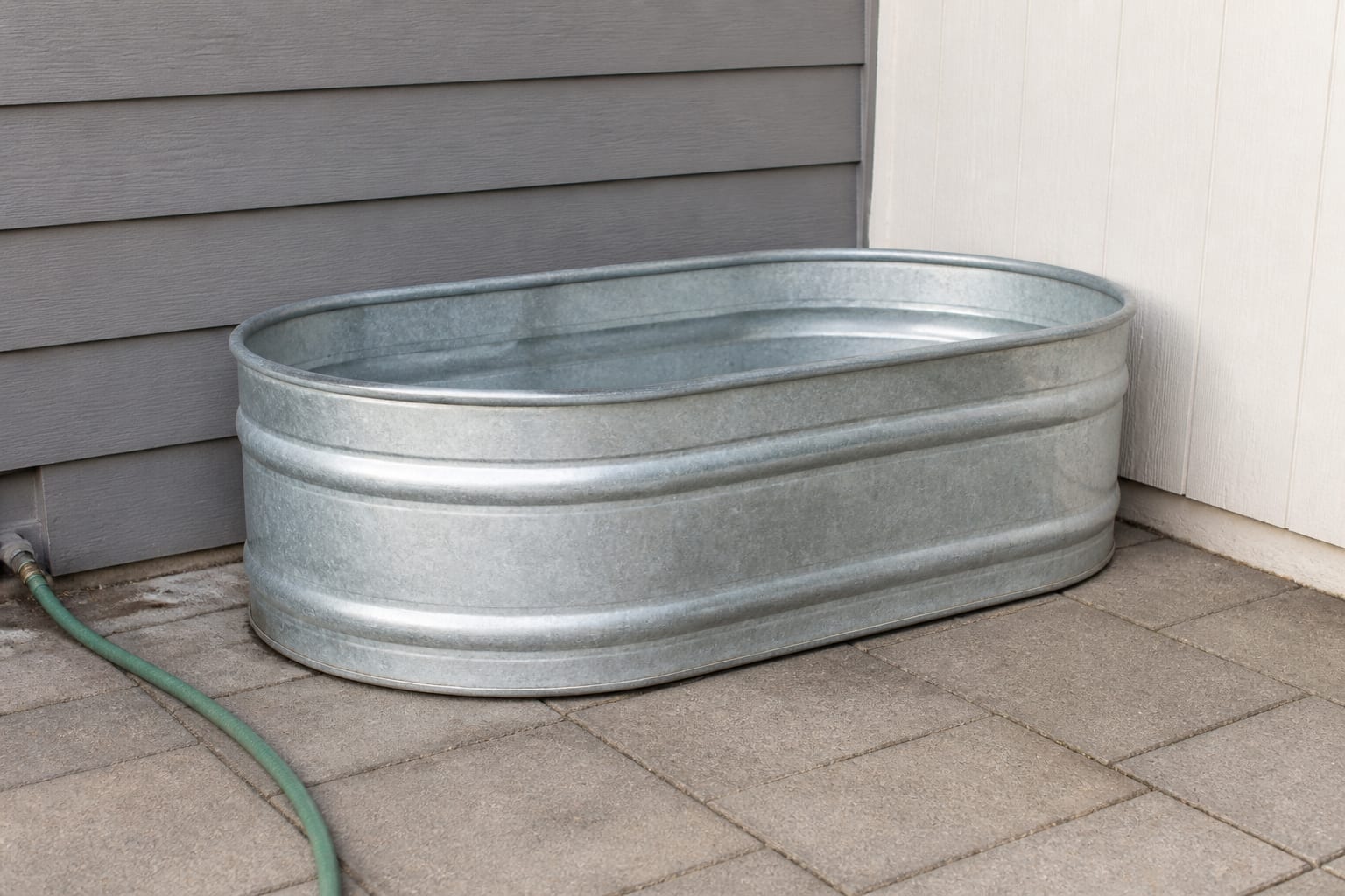 Bare patio corner with a plain galvanized stock tank sitting on concrete, no surrounding decor