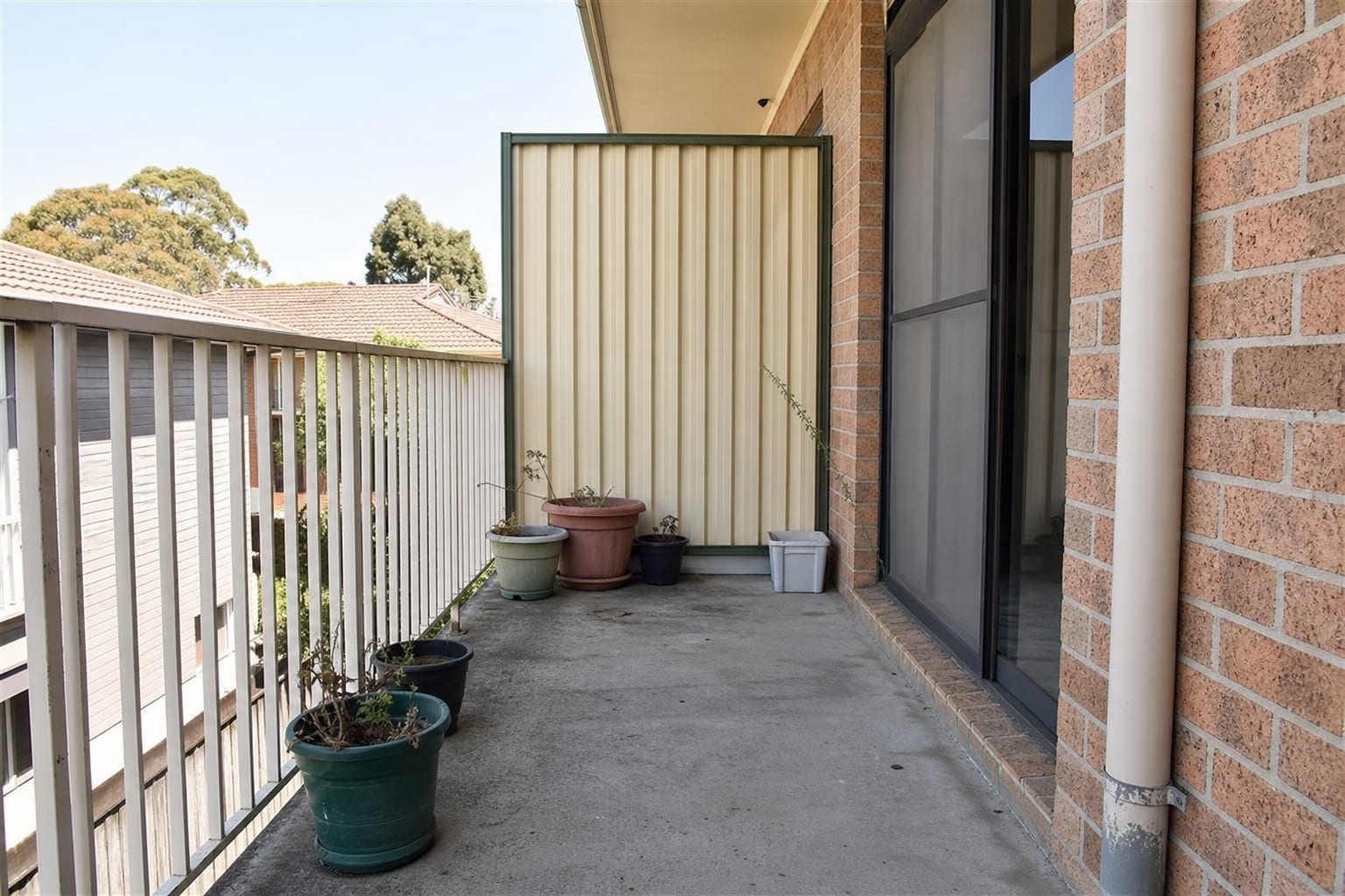 Narrow apartment balcony with a few small mismatched pots, bare railing, empty floor space, and no clear planting structure.