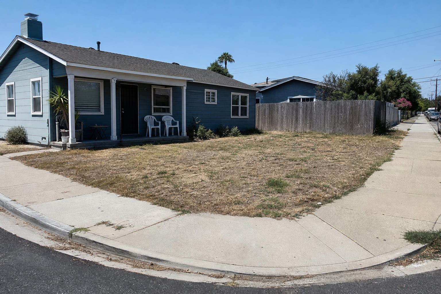 Corner lot front yard with bare lawn, exposed porch, no defined walkway, and two street edges visible from the intersection.