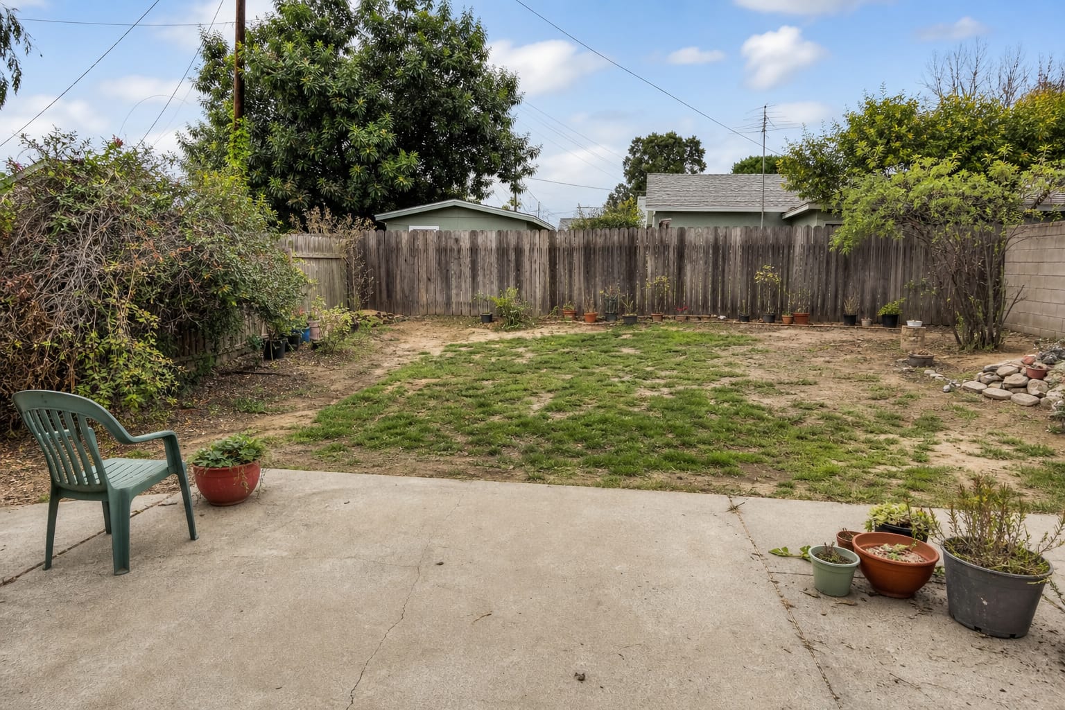 Plain rectangular backyard with patchy grass, exposed fence panels, narrow beds, and no seating or planted focal point.