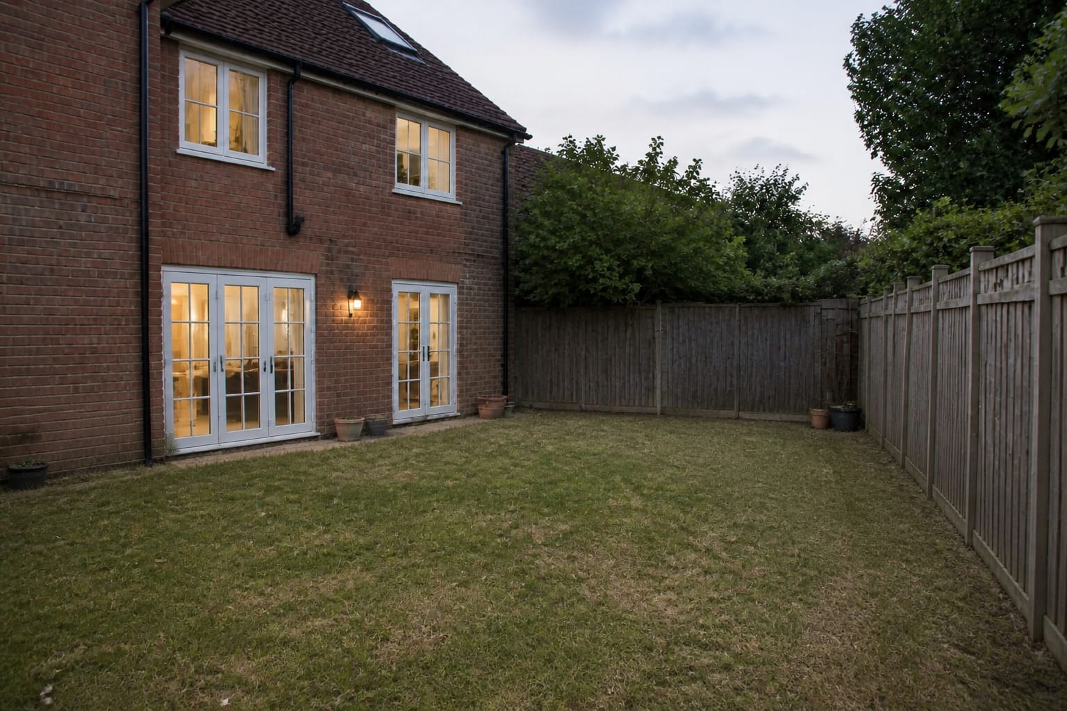 Plain rectangular lawn with narrow fence line, scattered pots, no path, no layered planting, and an unused back corner.
