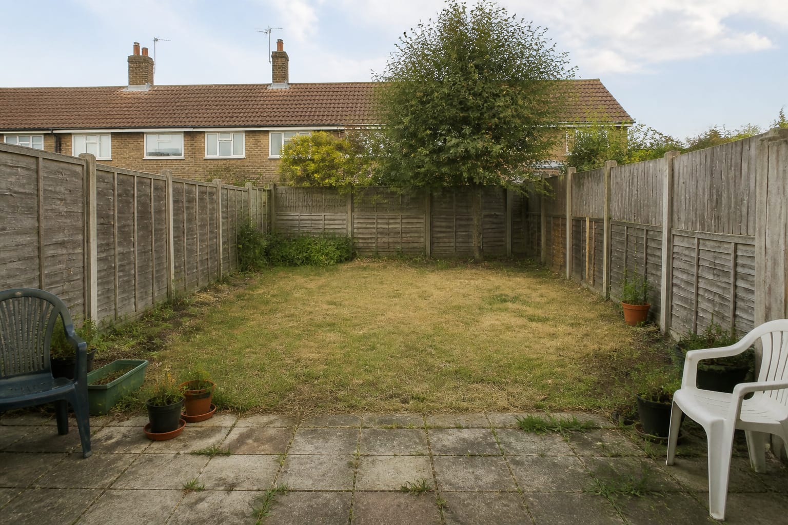 Plain rectangular lawn with narrow fence line, scattered pots, no path, no layered planting, and an unused back corner.