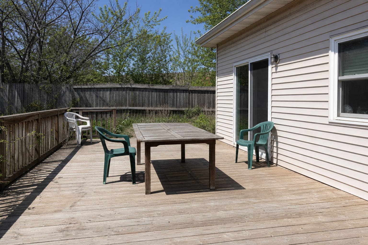 exposed backyard deck with hot sun, a bare table, scattered chairs, and no roof, shade, lighting, or privacy from nearby yards.