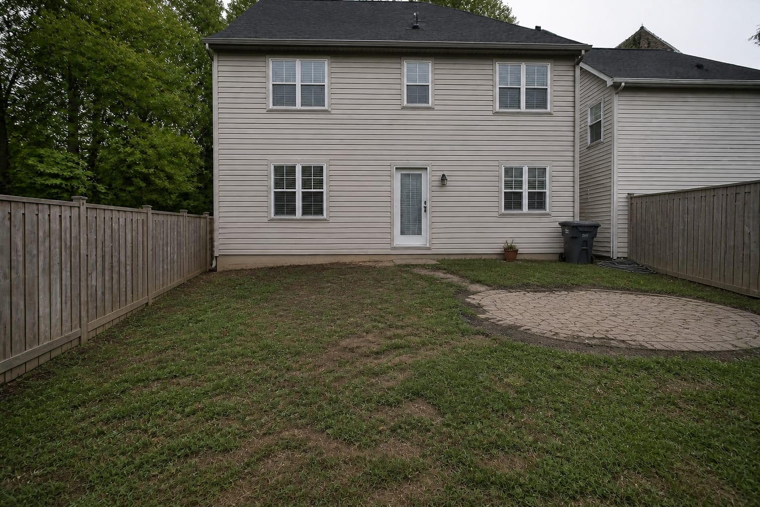 Bare patchy backyard lawn with no deck and a plain back door before the build