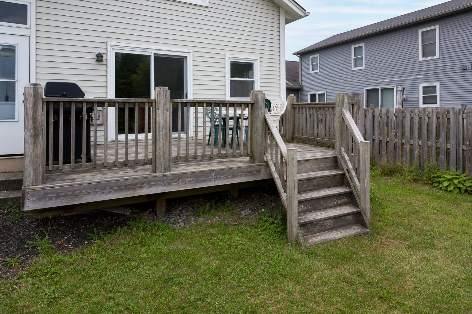 raised backyard deck with faded boards, bulky railing, a lonely grill, no lighting, and awkward stairs down to the lawn.