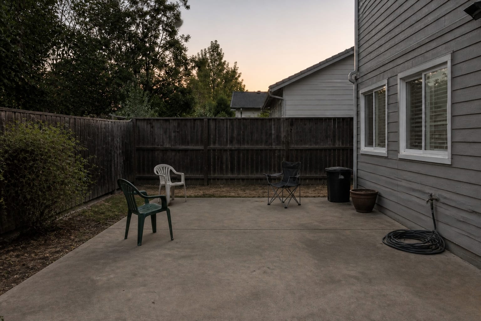 plain backyard patio corner with scattered folding chairs, a bare concrete slab, no lighting, and no defined fire pit zone