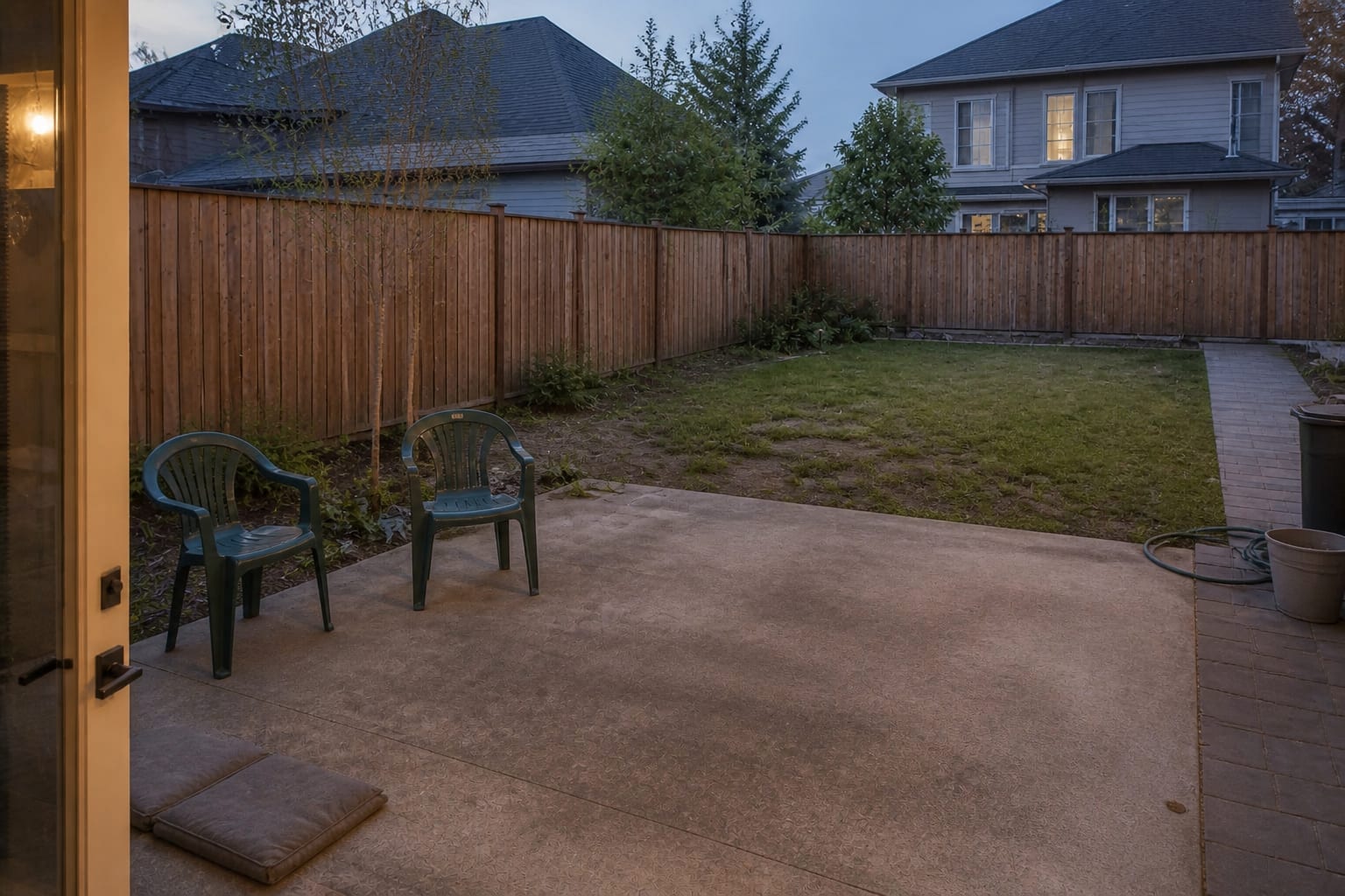 Plain backyard patio with exposed chairs, no overhead cover, no lighting plan, and loose cushions left near the door.
