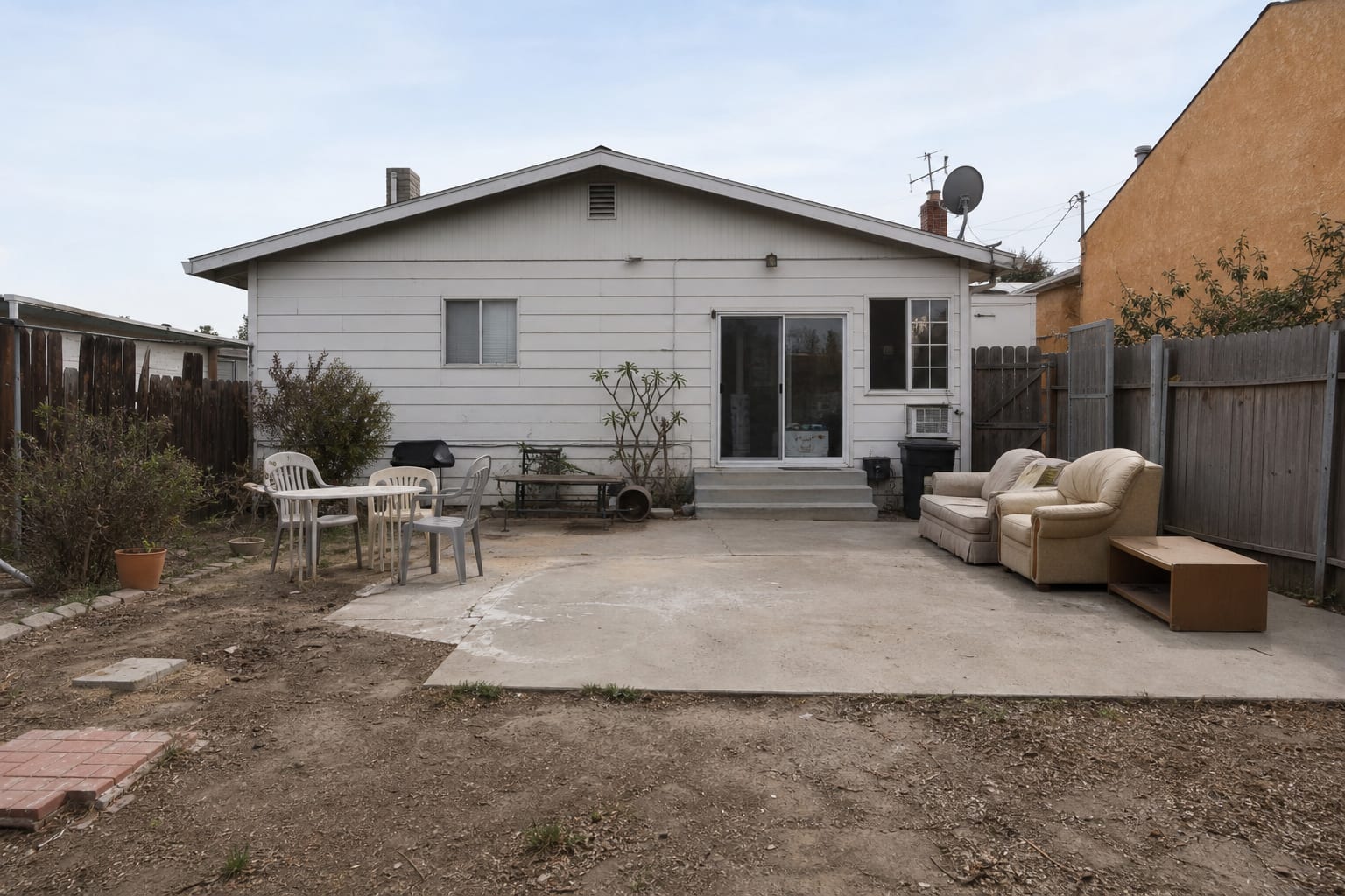 Plain beige house exterior with a faded white front door, small porch light, empty steps, and no strong focal point from the curb.