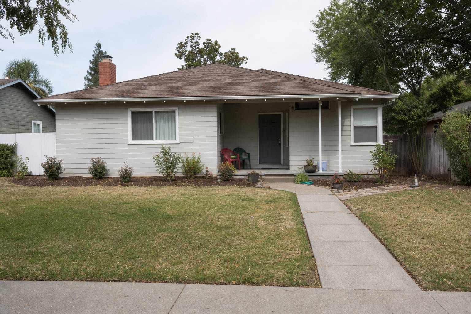 Front yard with a narrow foundation strip, scattered builder shrubs, bare mulch, and no clear planting rhythm beside the walkway.