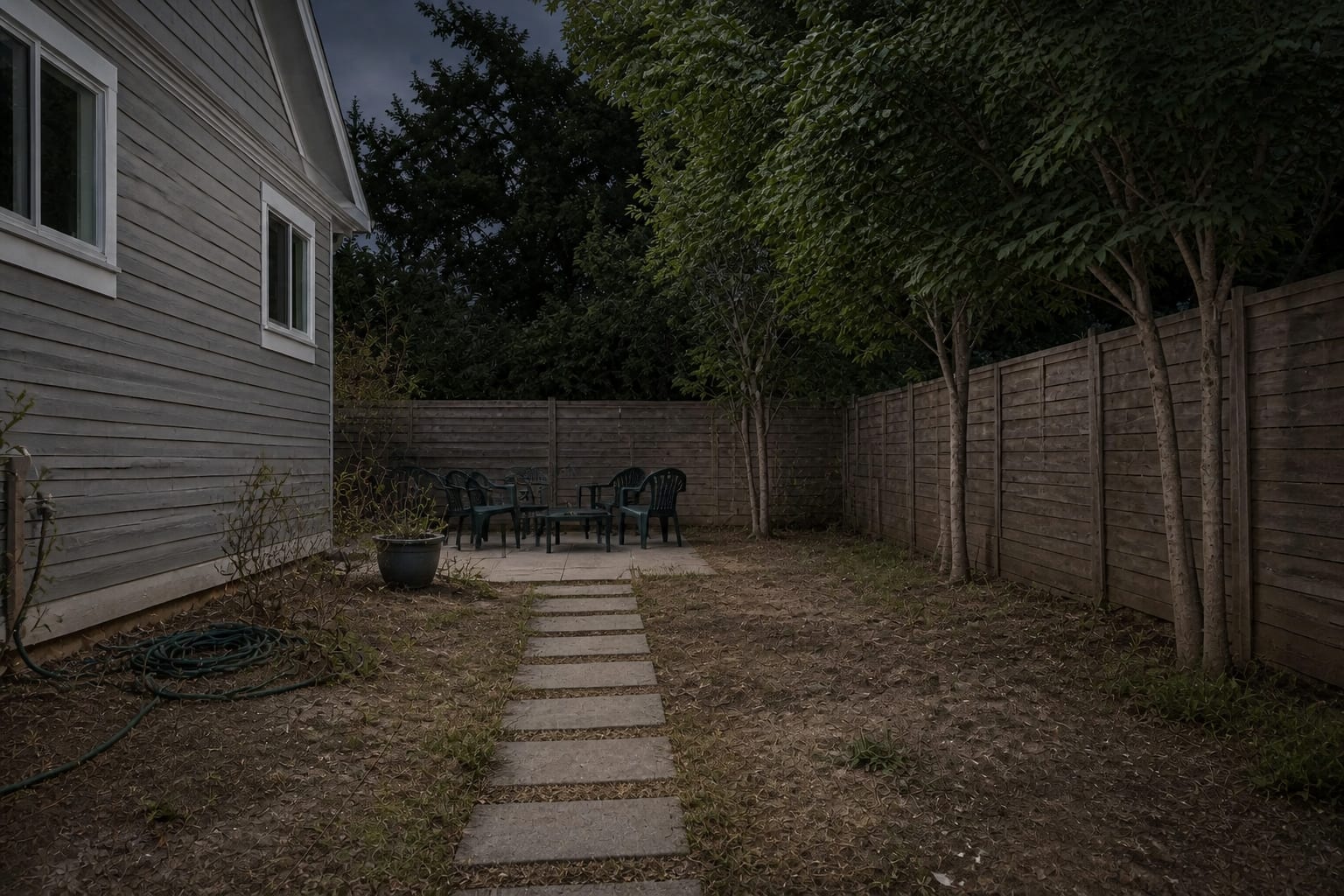 unlit garden path with dark planting beds, invisible steps, and a seating area disappearing into the yard after sunset