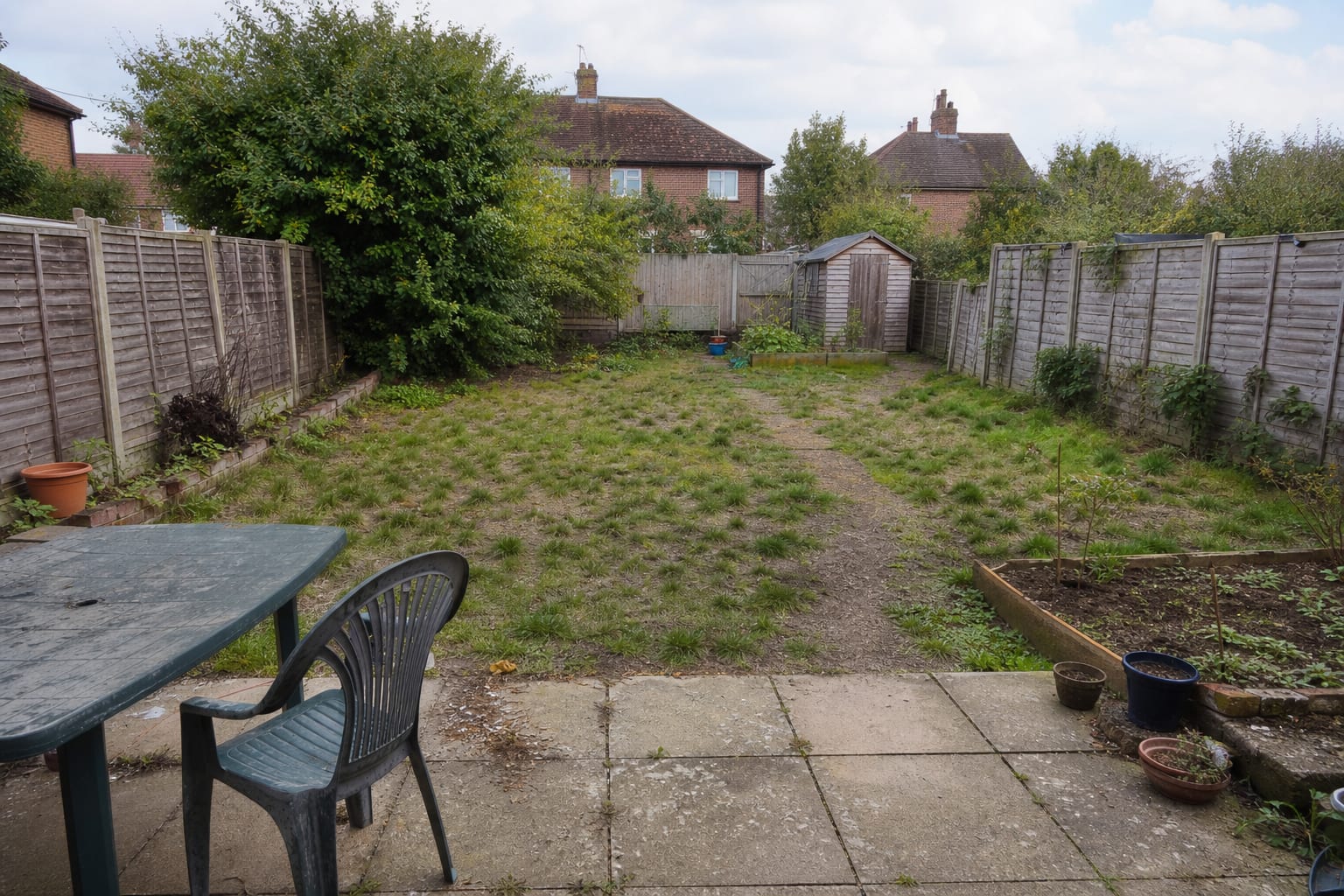 patchy lawn garden with an informal dirt shortcut, scattered pots, and no clear route between patio and planting beds