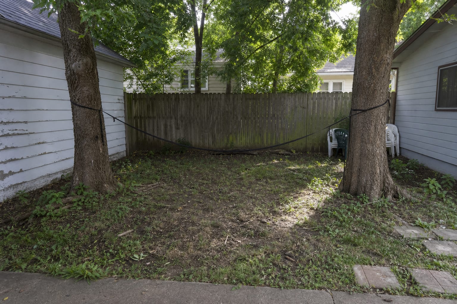 patchy backyard corner with two trees, bare soil, scattered toys, and no defined place to rest
