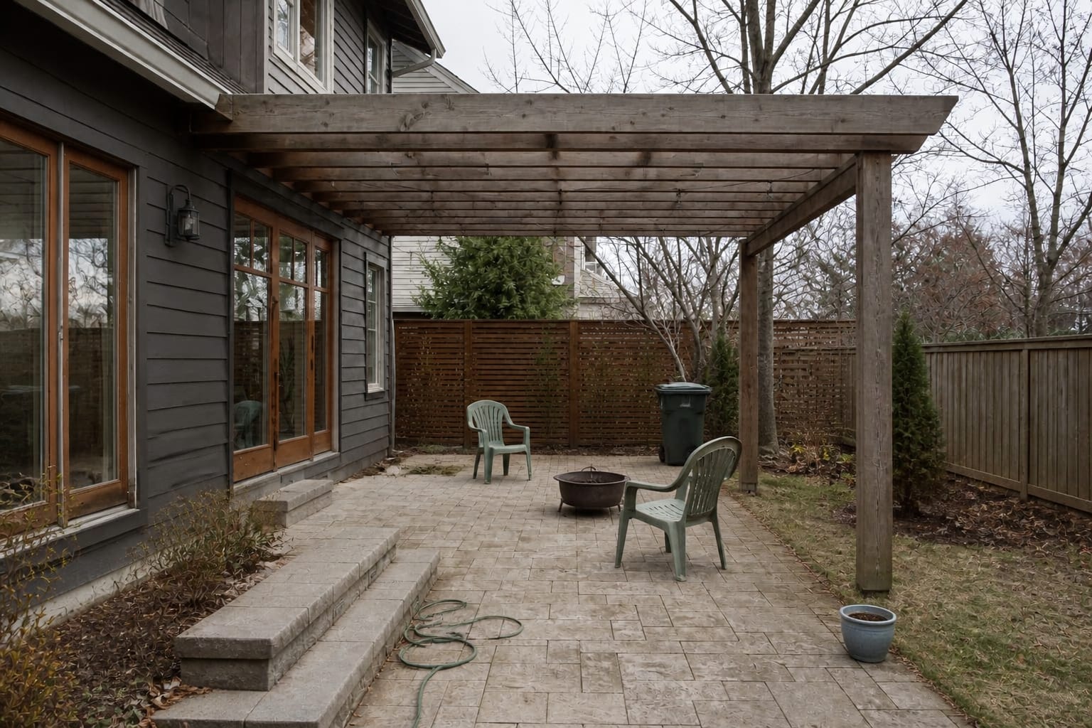 under designed pergola patio with scattered furniture, bare beams, exposed paving, and no heat or wind protection for cool evenings.