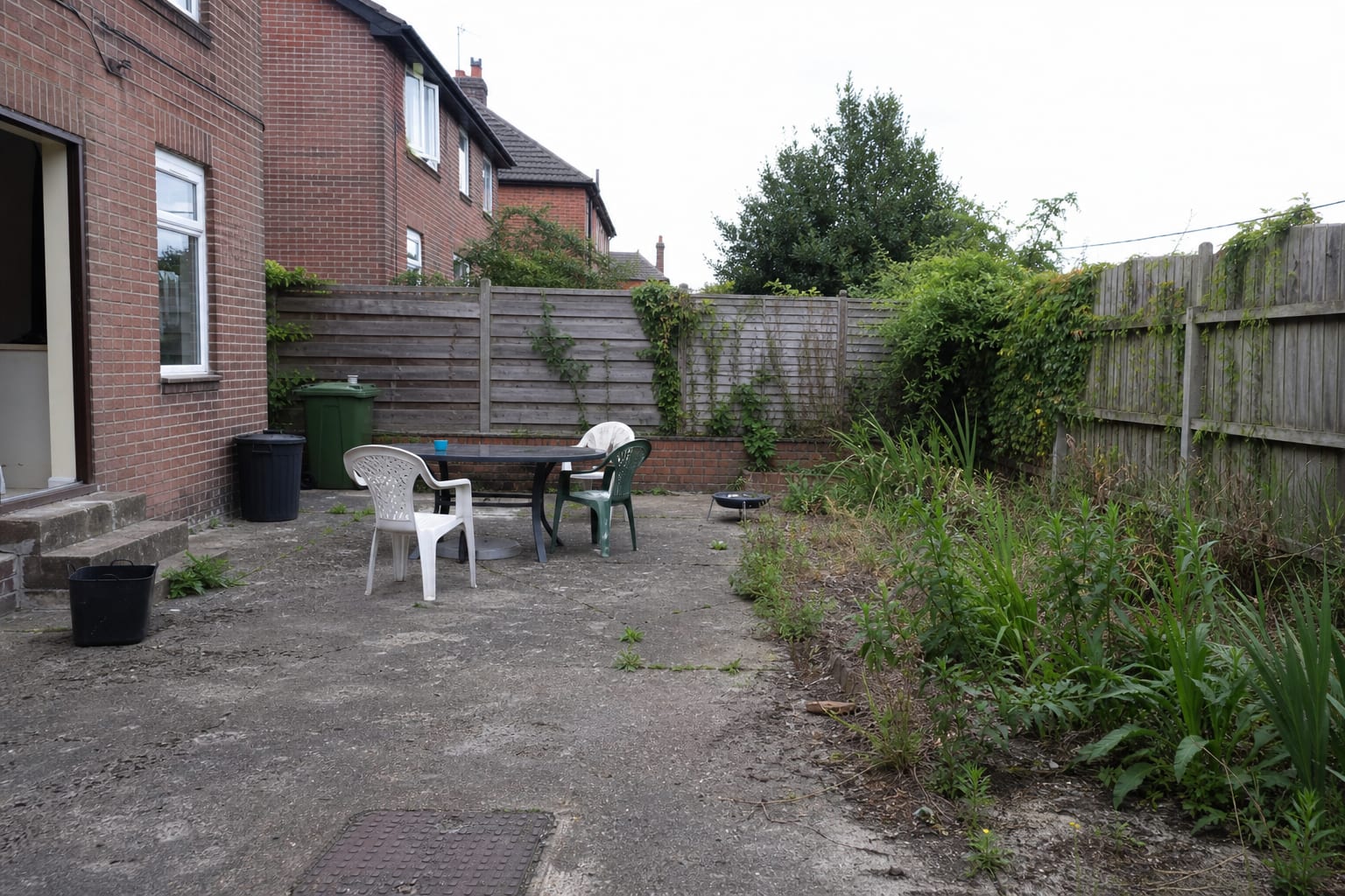 patio corner with mismatched herb pots, wet paving, leggy basil, and no clear route from the kitchen door.