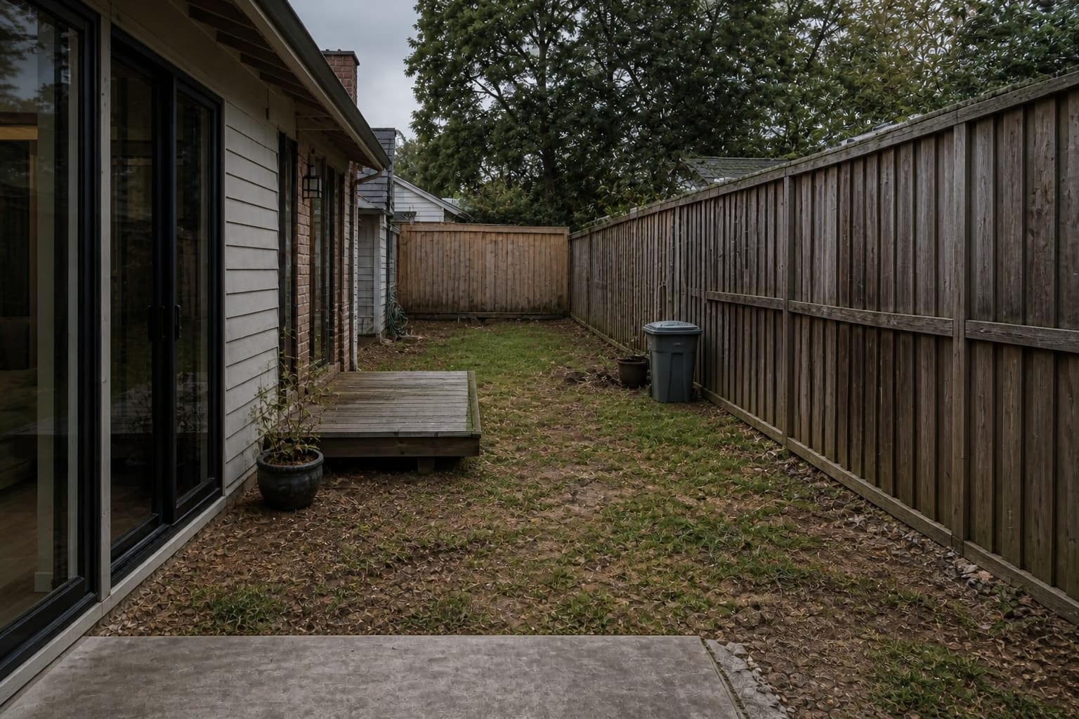 narrow backyard with patchy lawn, exposed fence panels, scattered pots, no focal point, and an awkward unused corner near the house.