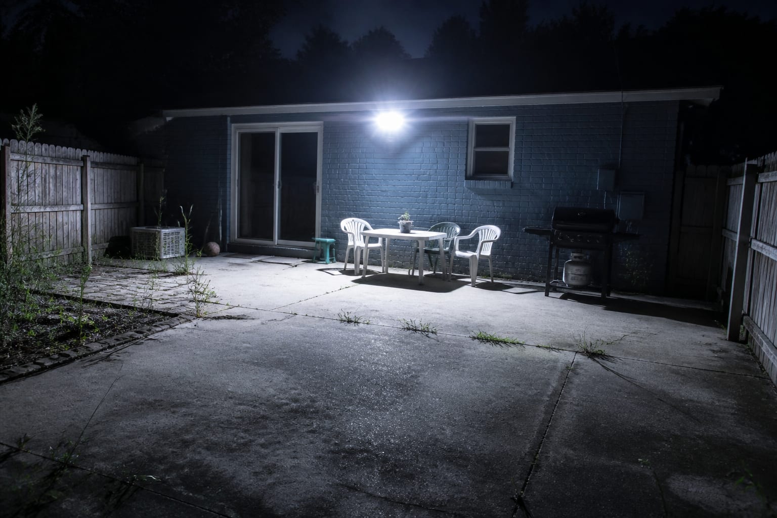 Backyard at night washed in harsh blue 5000K floodlight looking cold and flat before redesign