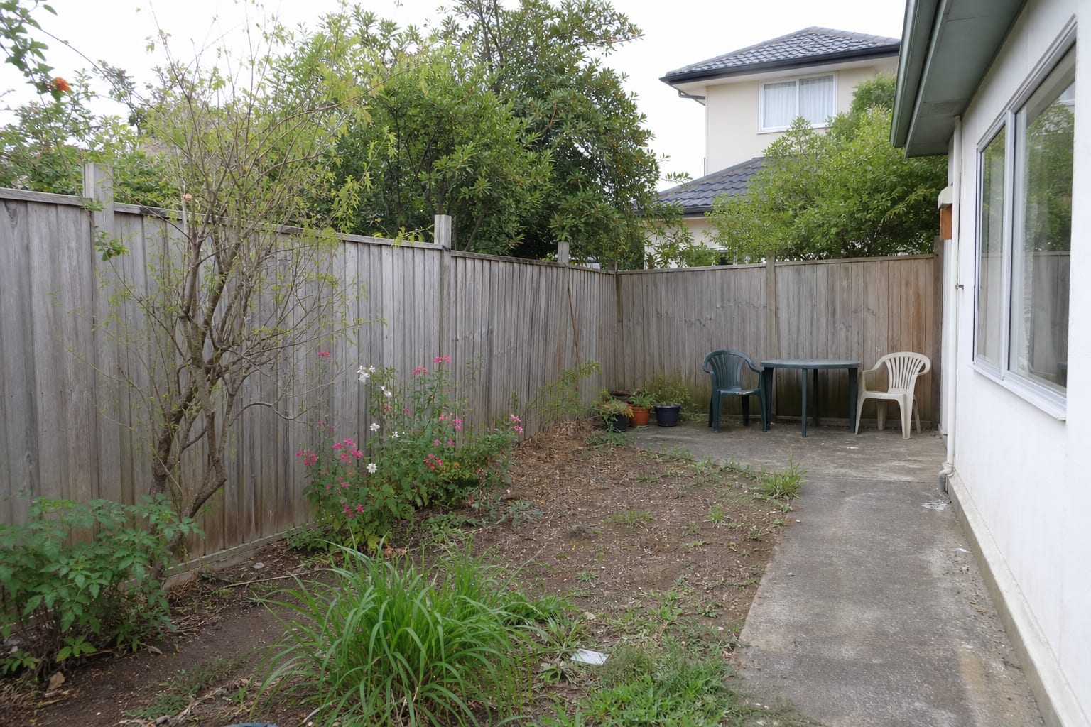 Under-designed garden boundary with a plain low fence, exposed neighbor view, sparse planting, and no clear privacy layer