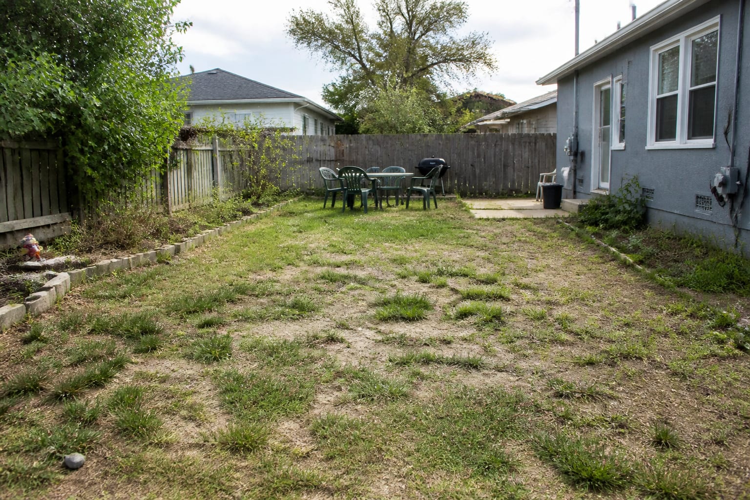 Patchy thin lawn with bare brown spots and weeds before a full-season care schedule