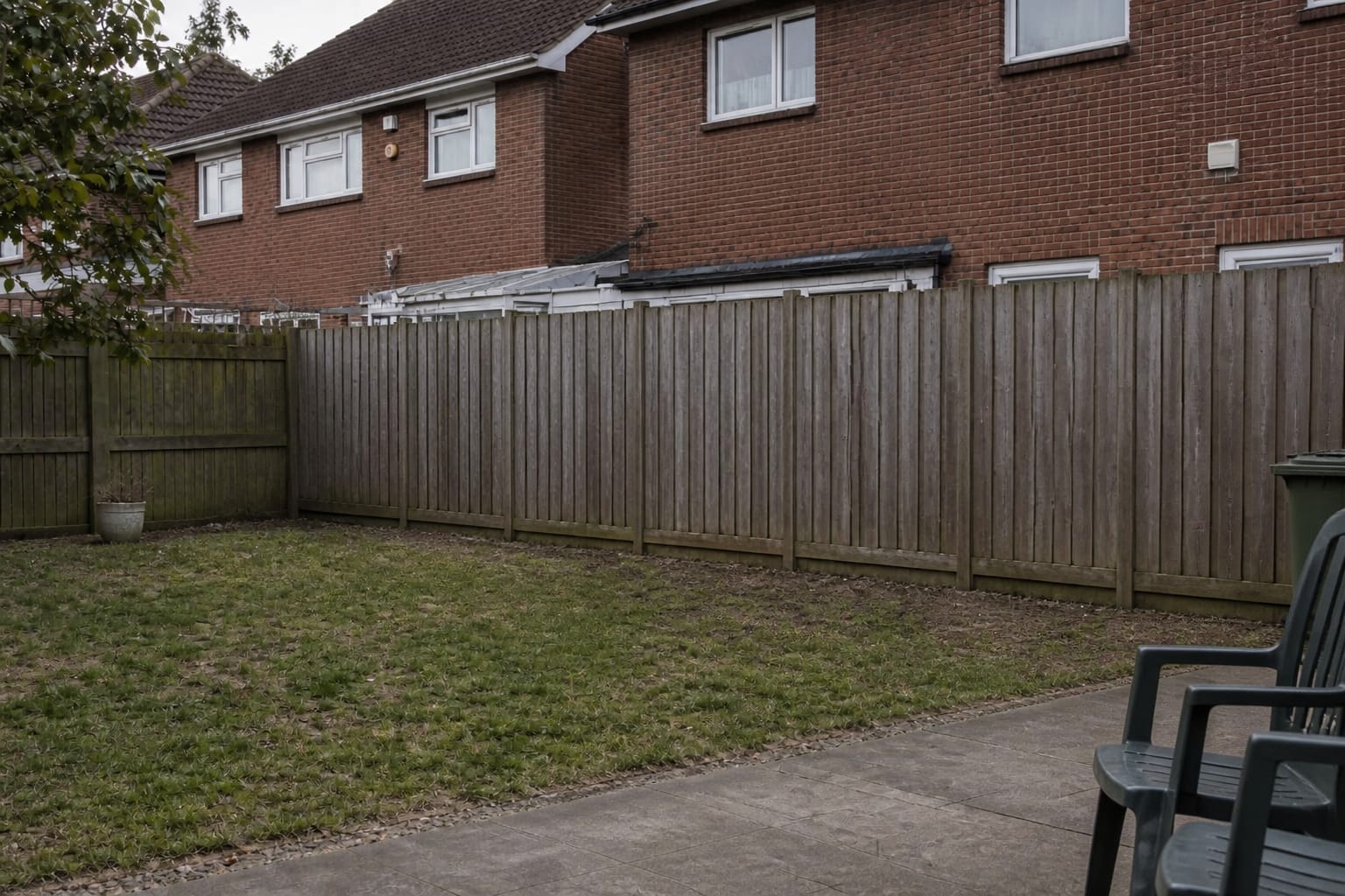 under designed garden boundary with a patchy lawn, exposed neighboring windows, scattered pots, and no planted privacy structure