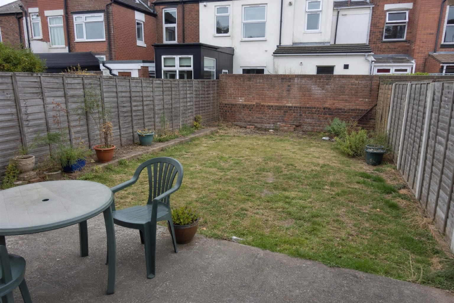 under designed garden boundary with a patchy lawn, exposed neighboring windows, scattered pots, and no planted privacy structure