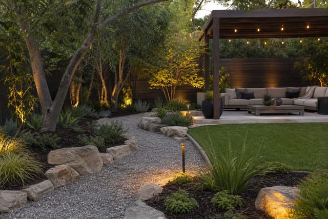 low-maintenance backyard with gravel paths, drought tolerant planting, mulch, and a shaded seating area beside a small lawn